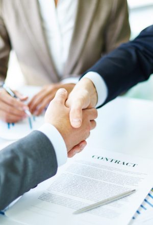 Image of business partners handshaking over business objects on workplace